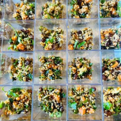 Recipientes cuadrados dispuestos en forma de cuadrícula, cada uno con una porción de ensalada de quinoa con verduras, pasas y hortalizas picadas, perfectos para catering de eventos gourmet o de team building en Barcelona que buscan una cocina fresca y creativa.