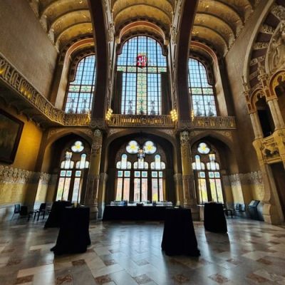 Gran salón con altos techos abovedados, vidrieras y columnas decorativas, ideal para eventos de team building en Barcelona o catering para reuniones gourmet. Varias mesas con manteles negros están dispuestas sobre un suelo de mármol estampado.