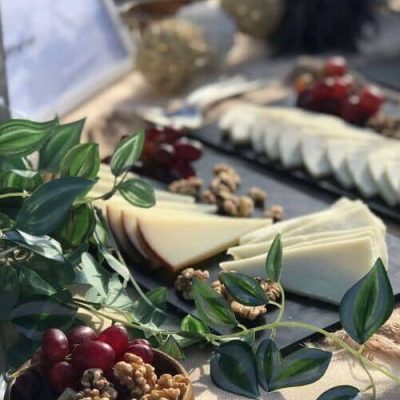 Una mesa con bandejas de queso en lonchas, racimos de uvas rojas, nueces y follaje verde, dispuestos para una exhibición de comida gourmet: inspiración perfecta para su próximo evento de Team Building en Barcelona.