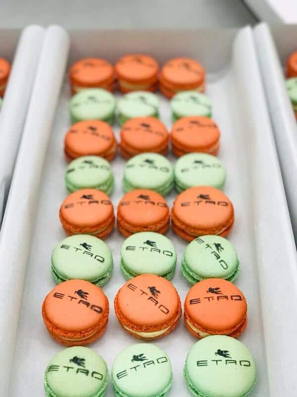 Una rebanada de reposteria y pasteleria creativa en capas con chocolate y crema en un plato gris, adornado con crema batida, dos bizcochos de soletilla, una frambuesa, menta y rociado con jarabe de chocolate.